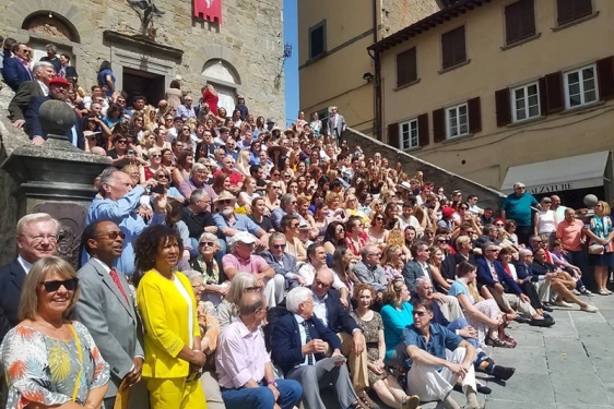 photo of a large group seated on sunny steps of a medieval palace.